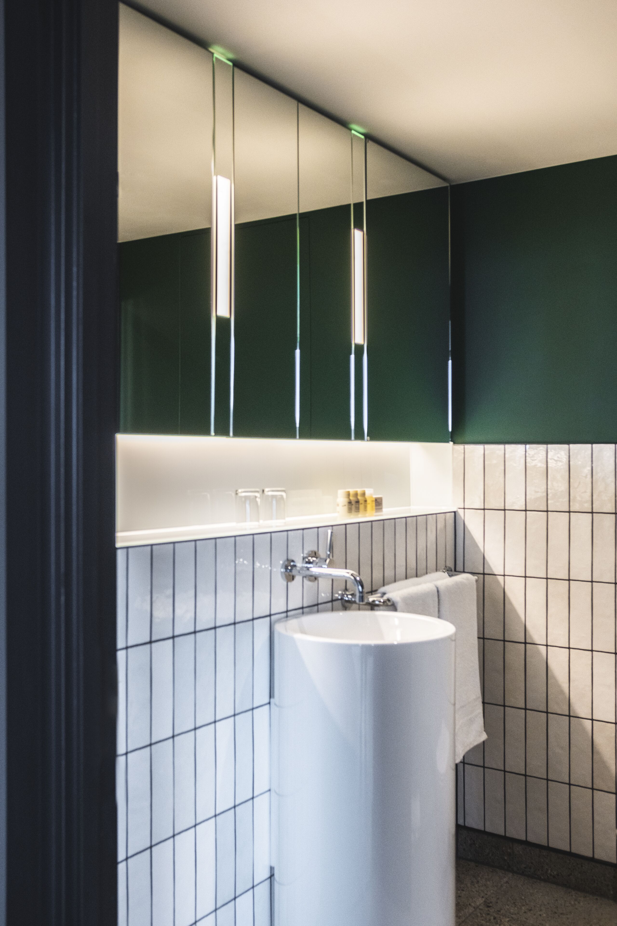 A bathroom with a white sink, green walls, and a mirror above the sink.
