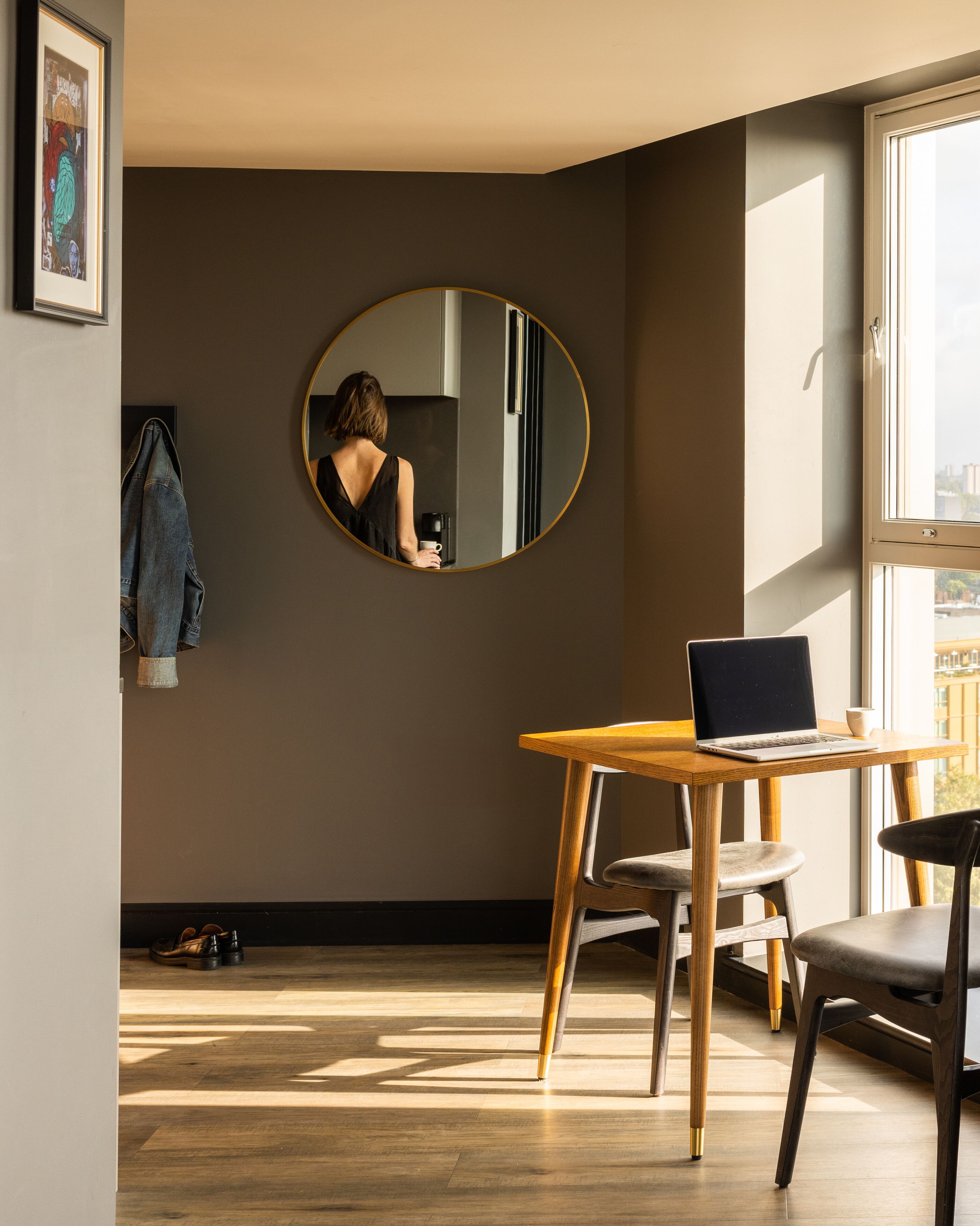 A modern room with a round mirror, a wooden table with a laptop, and a chair.