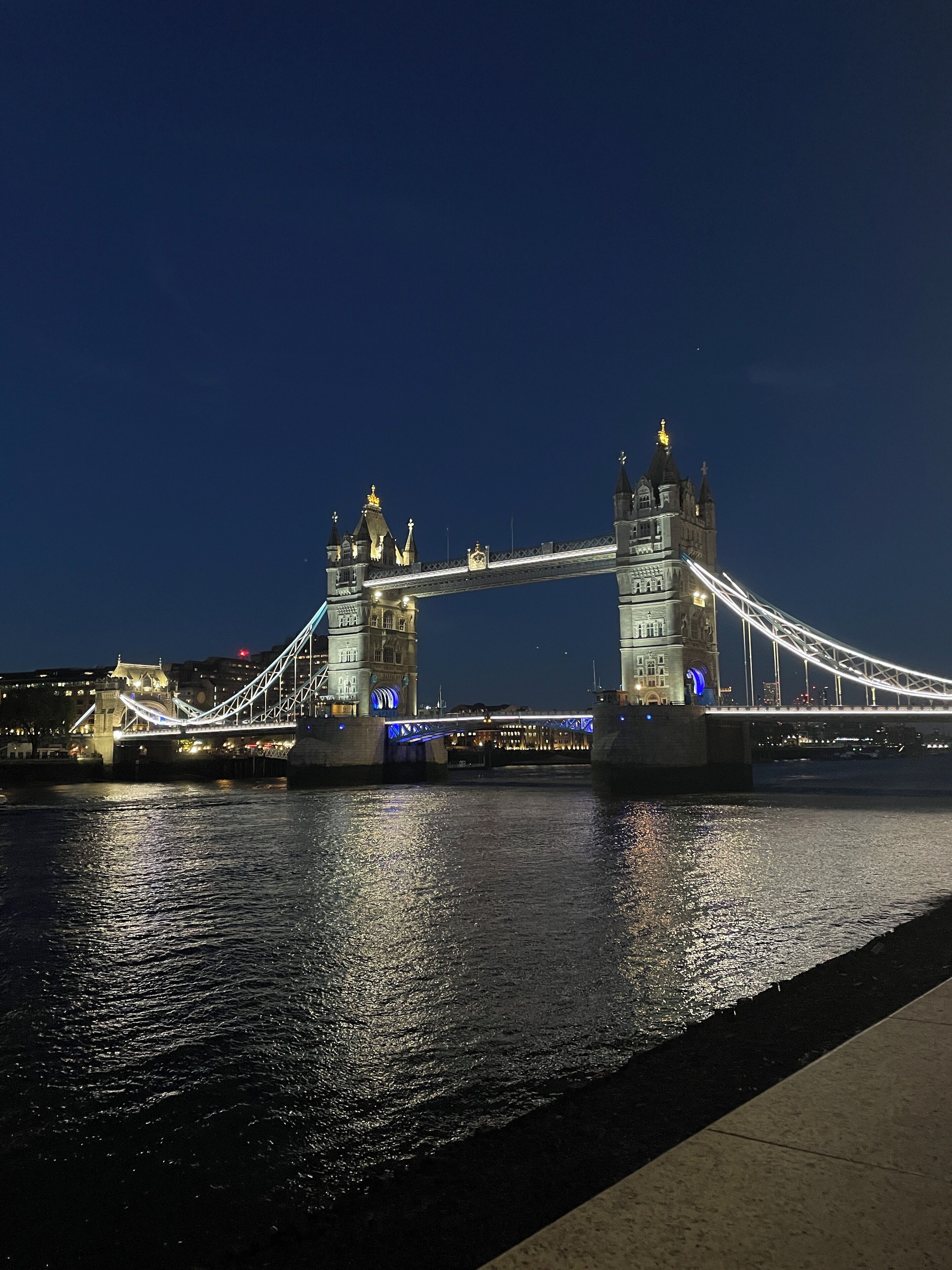 A nighttime view of a large suspension bridge with two towers, illuminated by lights, spanning over a body of water.