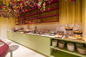 Een buffetgedeelte met diverse gerechten, een toonbank met borden en bestek, en een decoratief plafond met hangende bloemen.