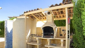 Ein Außenküchenbereich mit Steinboden, Pizzaofen und einer Pergola.