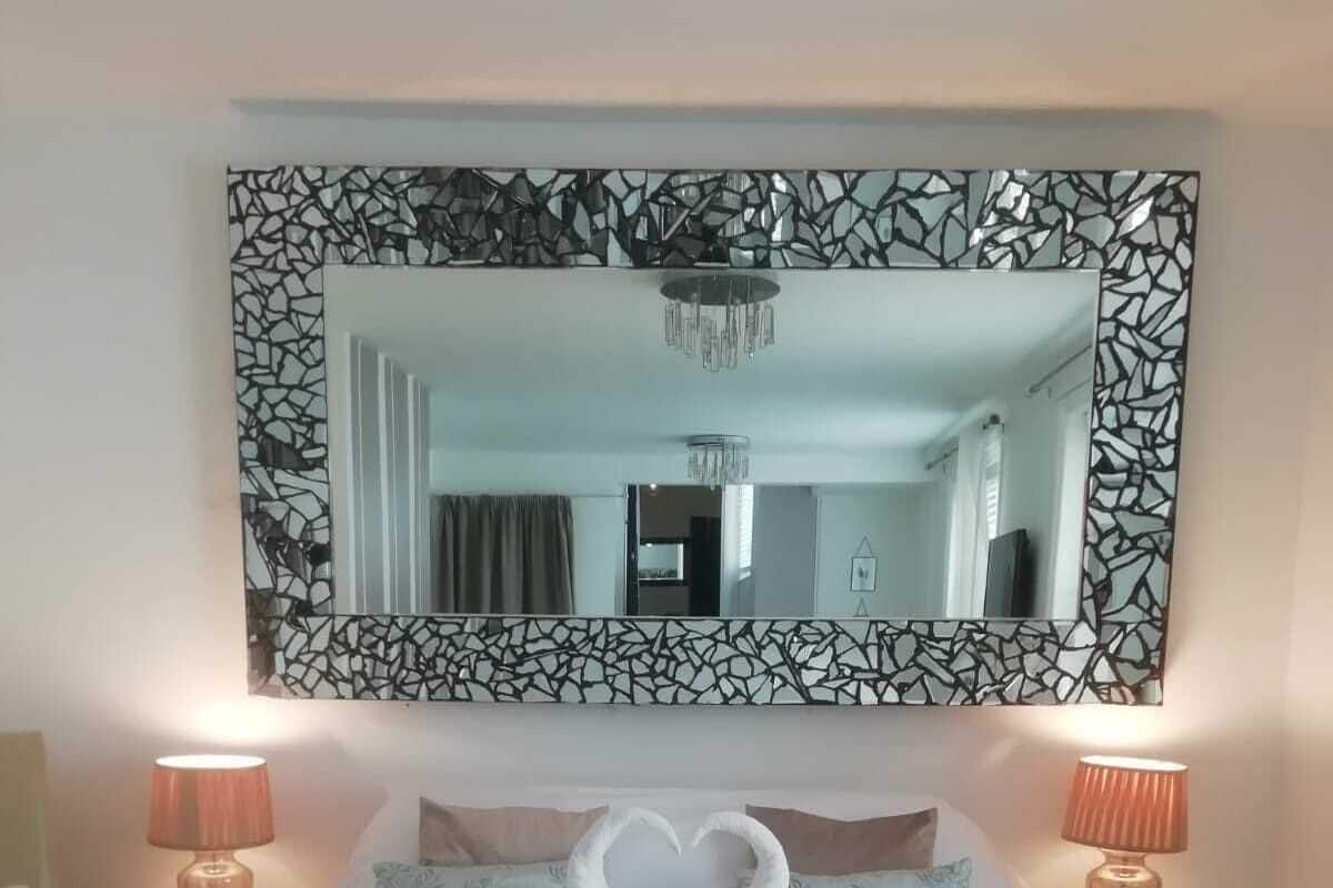 A neatly made bed with towels arranged in a heart shape, a large mirror with a mosaic frame, and two bedside lamps.