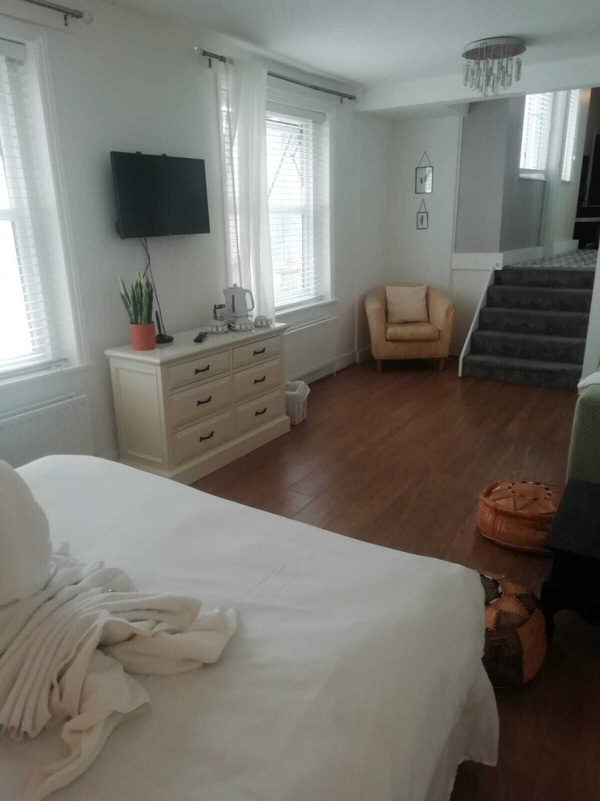 Ein Schlafzimmer mit Bett, Kommode, Stuhl und einer Treppe, die auf einen Balkon führt.