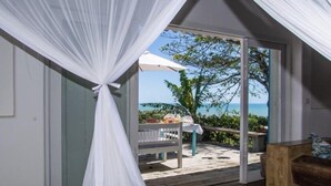 A bedroom with a canopy bed, a sliding glass door leading to a deck with a table and chairs, and a view of the ocean. - Pousada Segredos de Trancoso (Porto Seguro)