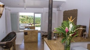 A spacious room with a wooden bathtub, a wooden bench, a small table, and a vase with flowers. - Pousada Segredos de Trancoso (Porto Seguro)