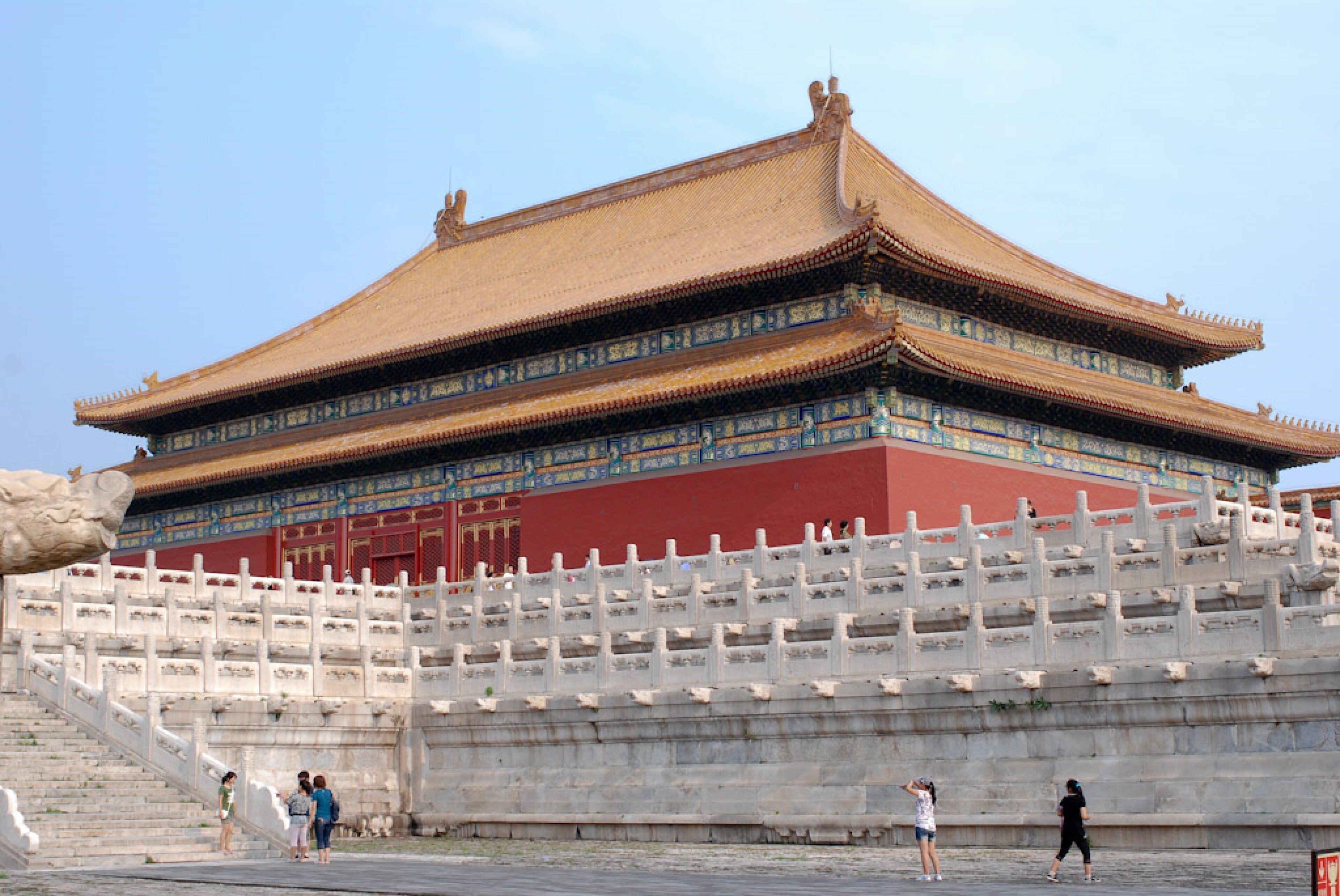 A large, traditional building with a prominent roof and a stone wall in front.