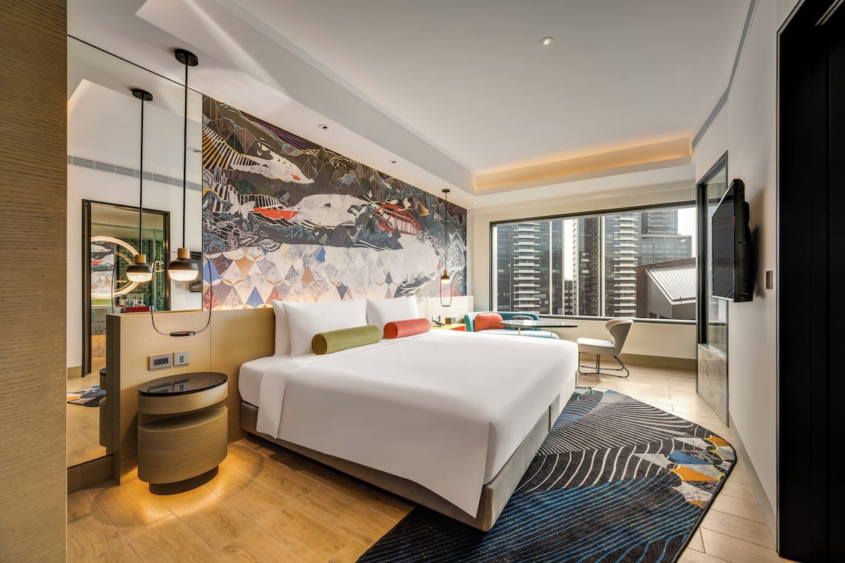 A modern hotel room with a large bed, a flat-screen TV, a large window with a city view, and a decorative wall mural.