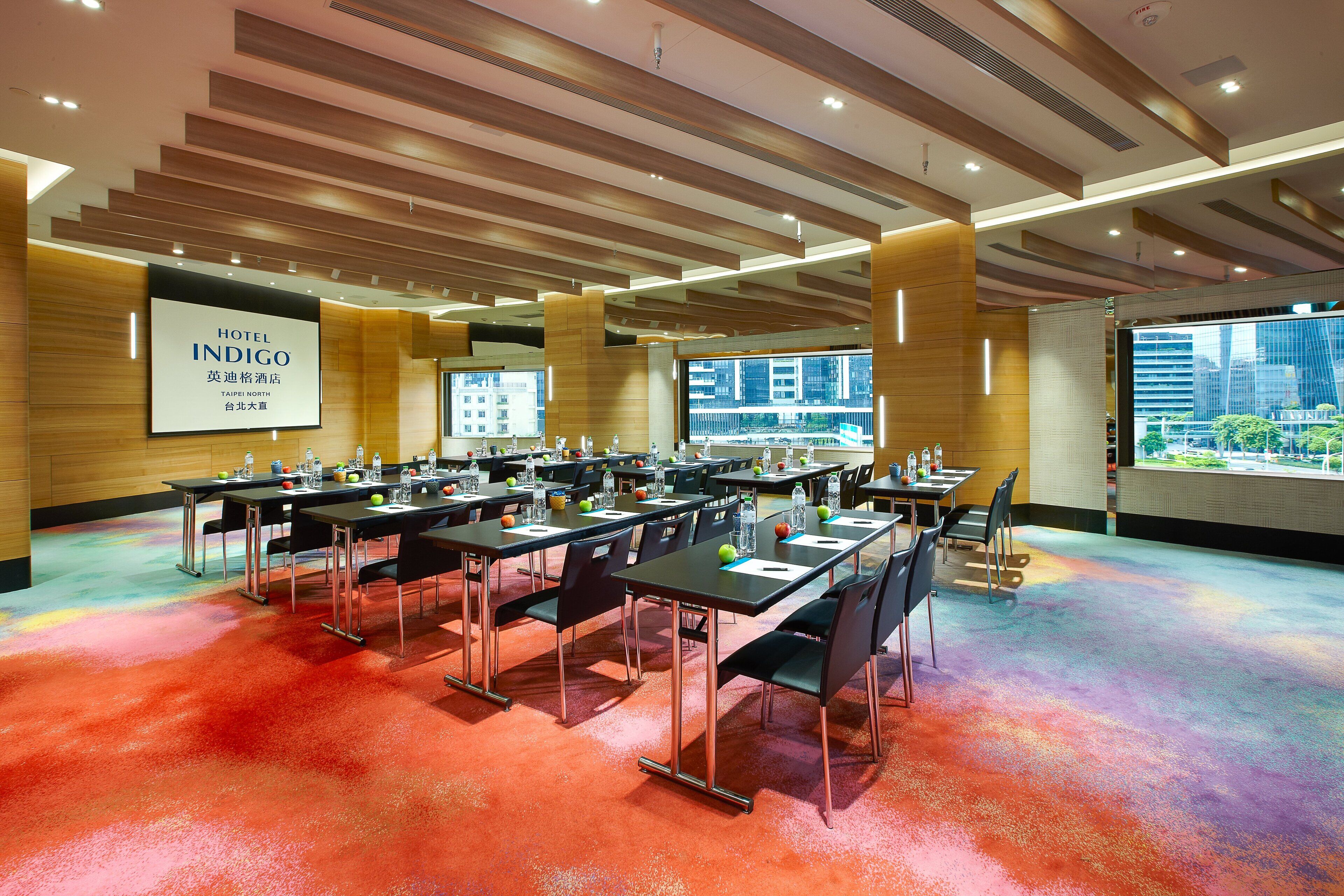 A hotel conference room with multiple tables, chairs, and a large screen displaying the hotel name.