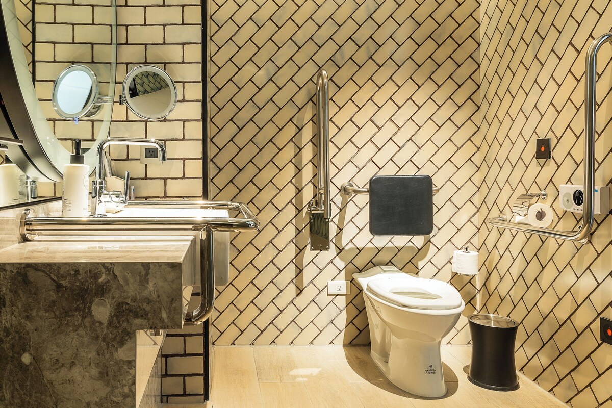Ein Badezimmer mit gefliestem Boden, einem Waschbecken mit Spiegel, einer Toilette und einem Mülleimer.