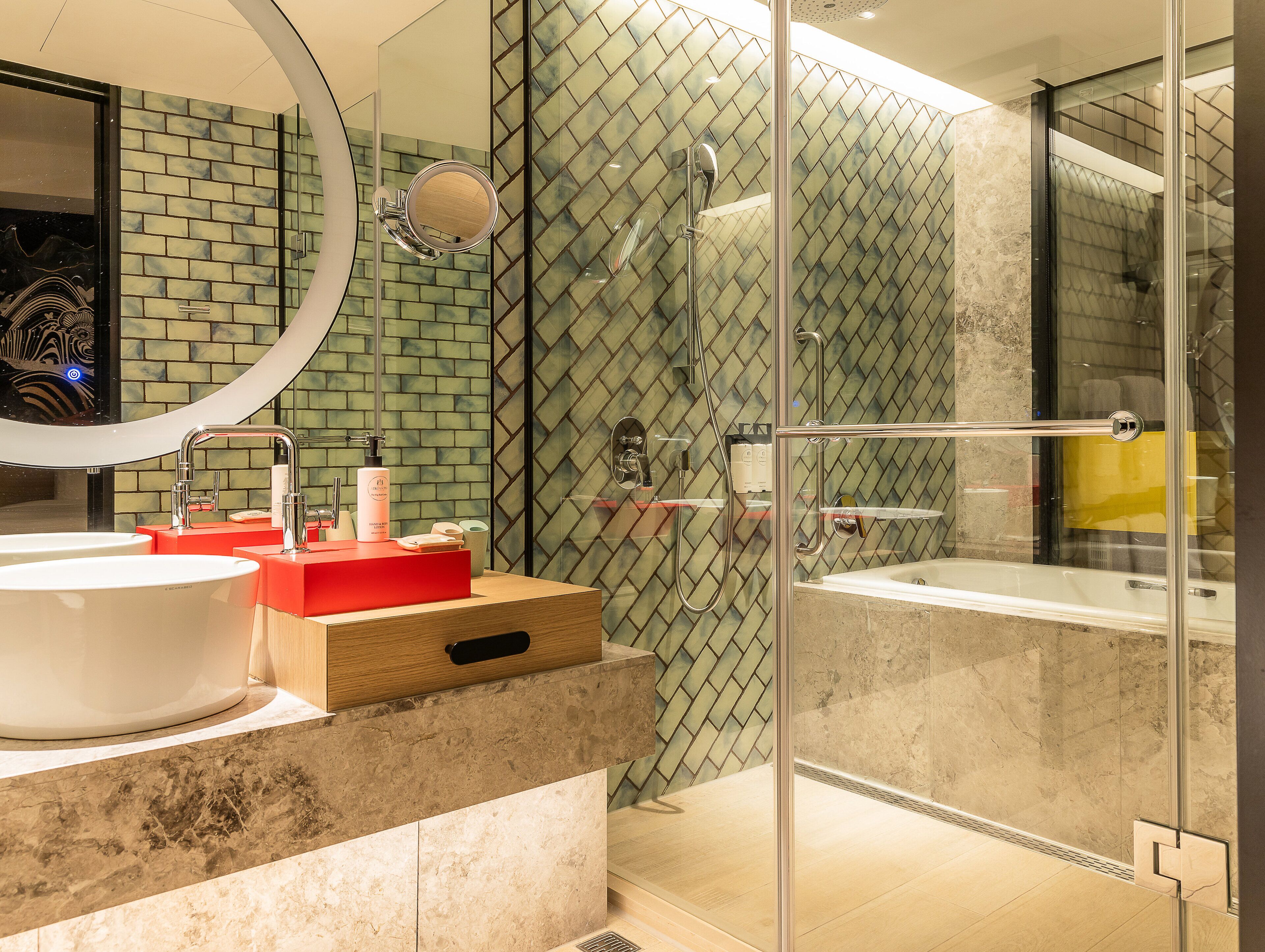 Een moderne badkamer met een groot wastafelmeubel, een douche met glazen wand en een spiegel met ronde rand.