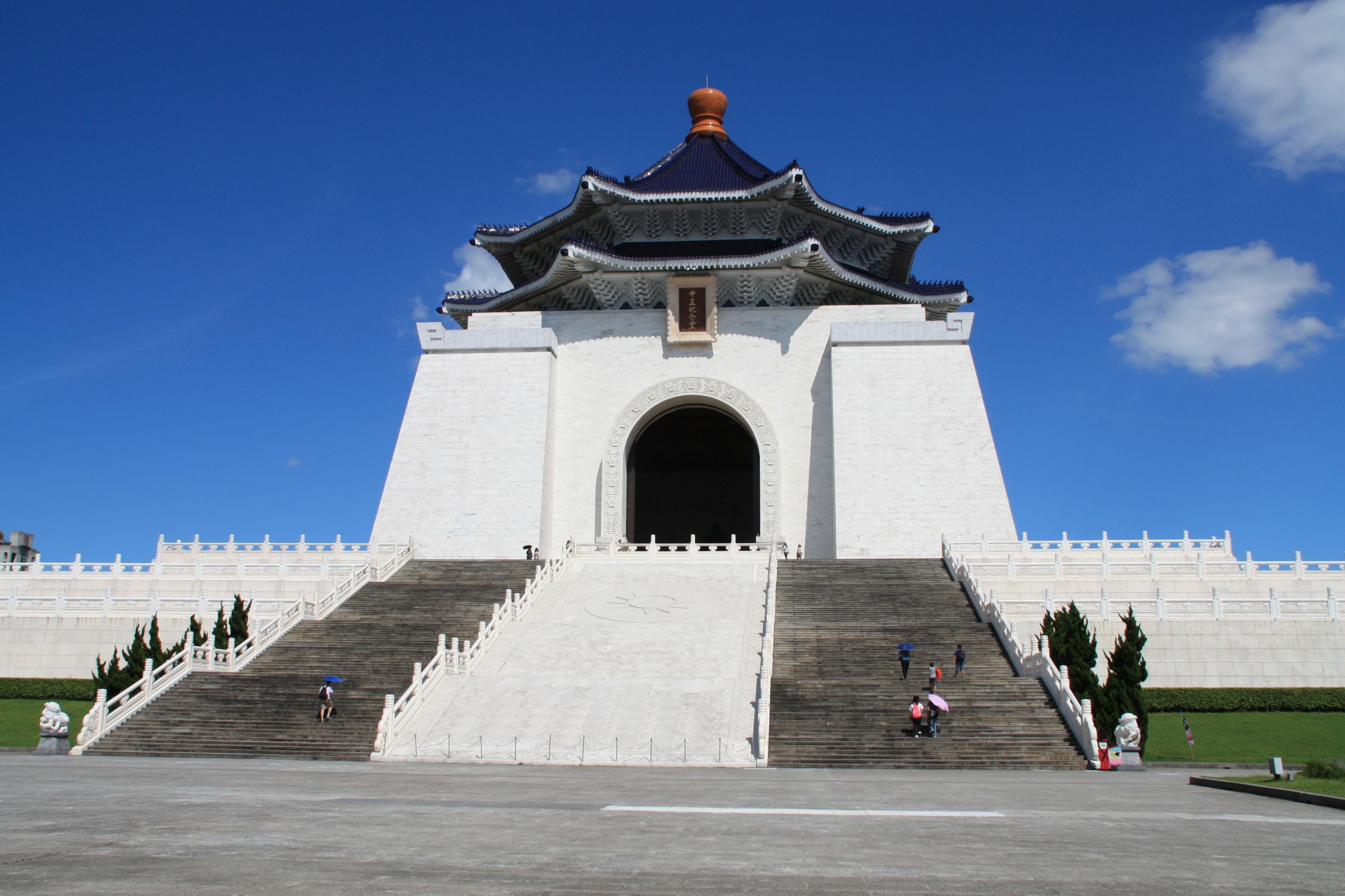 A large white building with a traditional roof and a central archway, flanked by wide steps leading up to it.