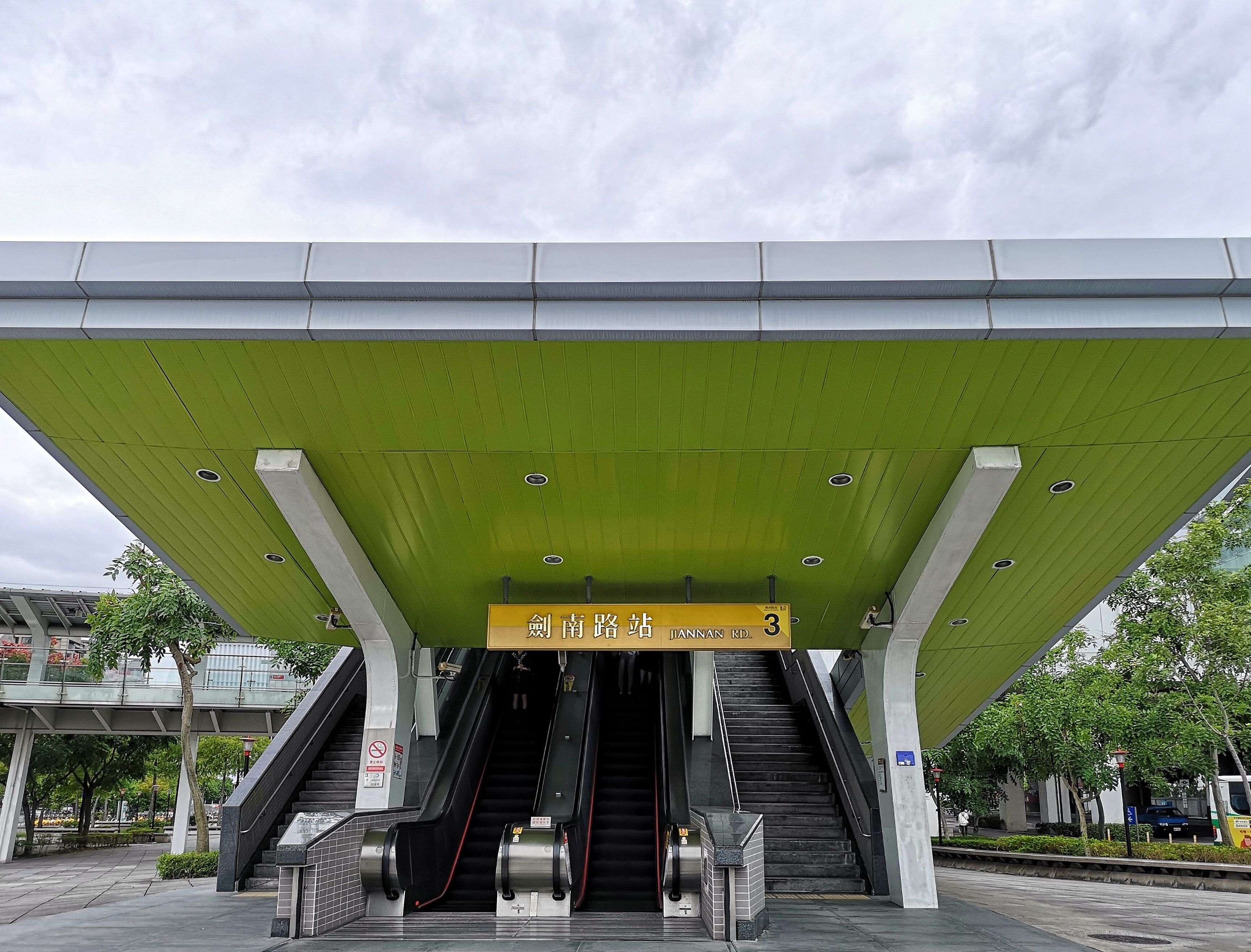A modern train station with a green roof and two escalators leading to a platform.