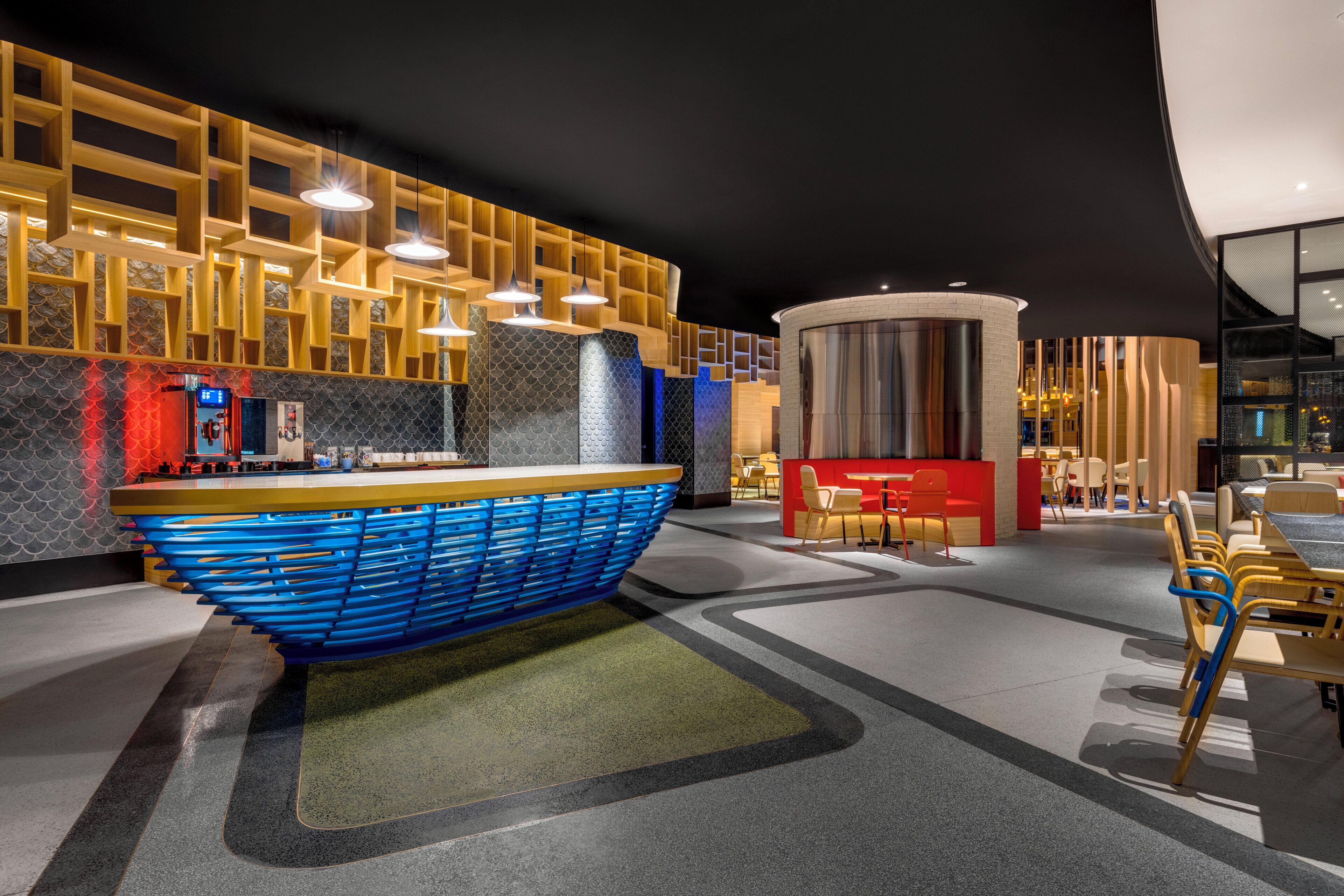 A modern interior with a central blue boat-shaped structure, wooden shelving, and a seating area with red and yellow chairs.