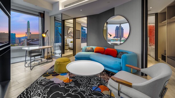 Ein modernes Wohnzimmer mit einem blauen Sofa, einem runden Spiegel und Blick auf eine Skyline bei Sonnenuntergang.