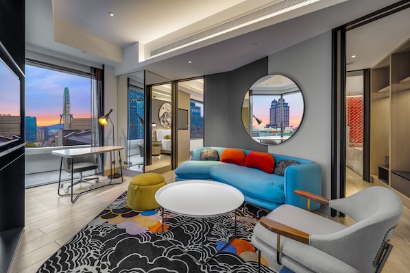 Een moderne woonkamer met een blauwe bank, een ronde spiegel en uitzicht op een stadshemel bij zonsondergang.
