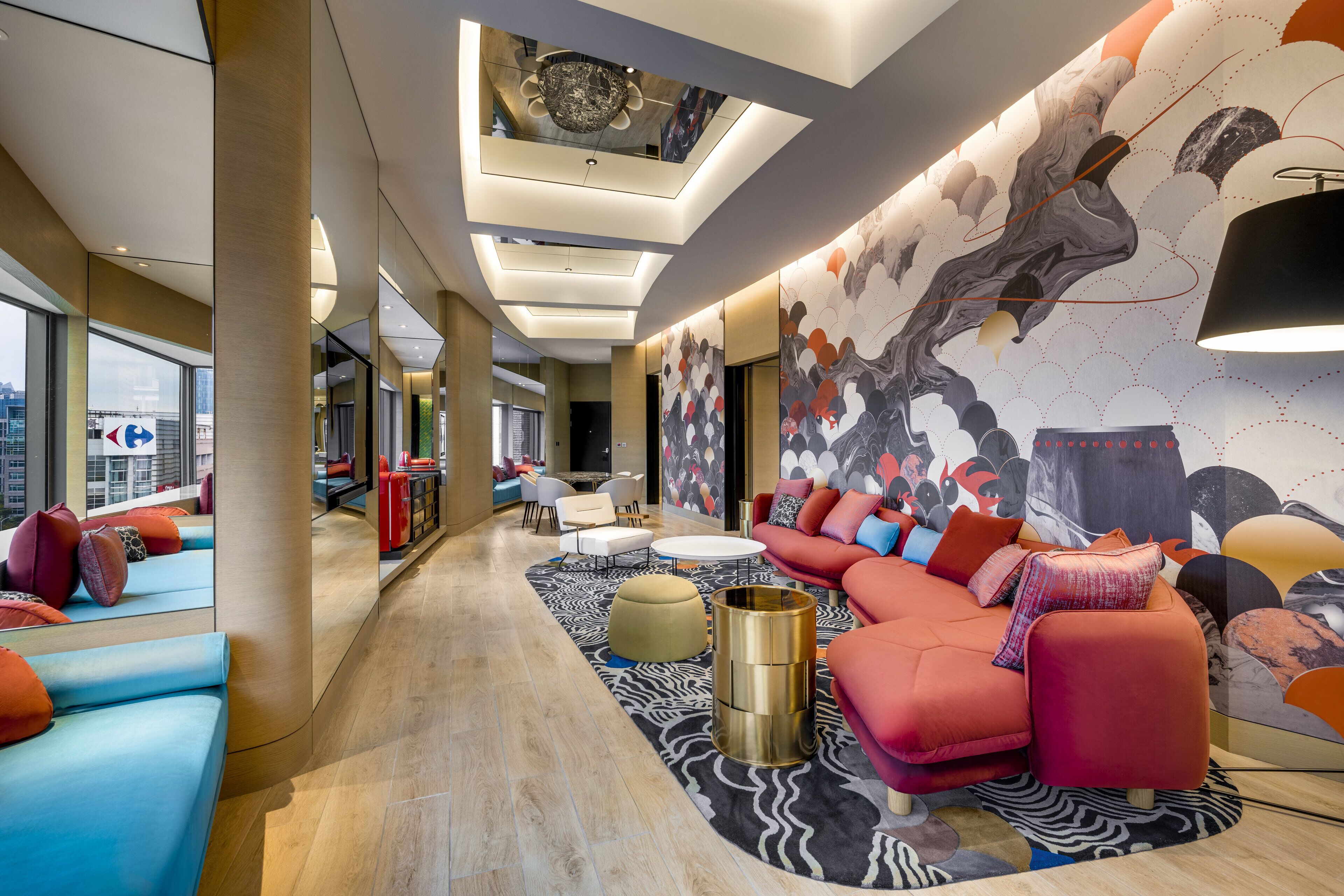 A modern hotel lobby with a long seating area, a large mural, and a high ceiling with skylights.