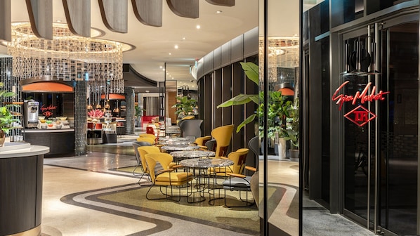 A modern cafe with round tables and yellow chairs, a coffee machine, and a neon sign.