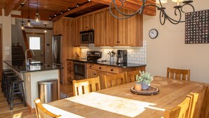 A kitchen with wooden cabinets, a stainless steel refrigerator, a microwave, and a sink. There is a dining table with chairs and a potted plant on the table. - 1320 Tennis Townhome 3 Bedroom Townhouse by RedAwning (Keystone)