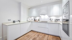 A modern kitchen with white cabinetry, a wooden floor, and built-in appliances. - Two bedroom apartment with sofa bed (London)