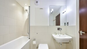 A modern bathroom with a bathtub, toilet, sink, and mirror. - Two bedroom apartment with sofa bed (London)
