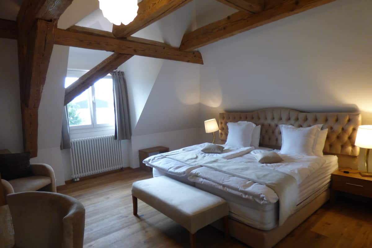 Une chambre avec un grand lit, un plafond en bois, une fenêtre avec des rideaux et un radiateur.