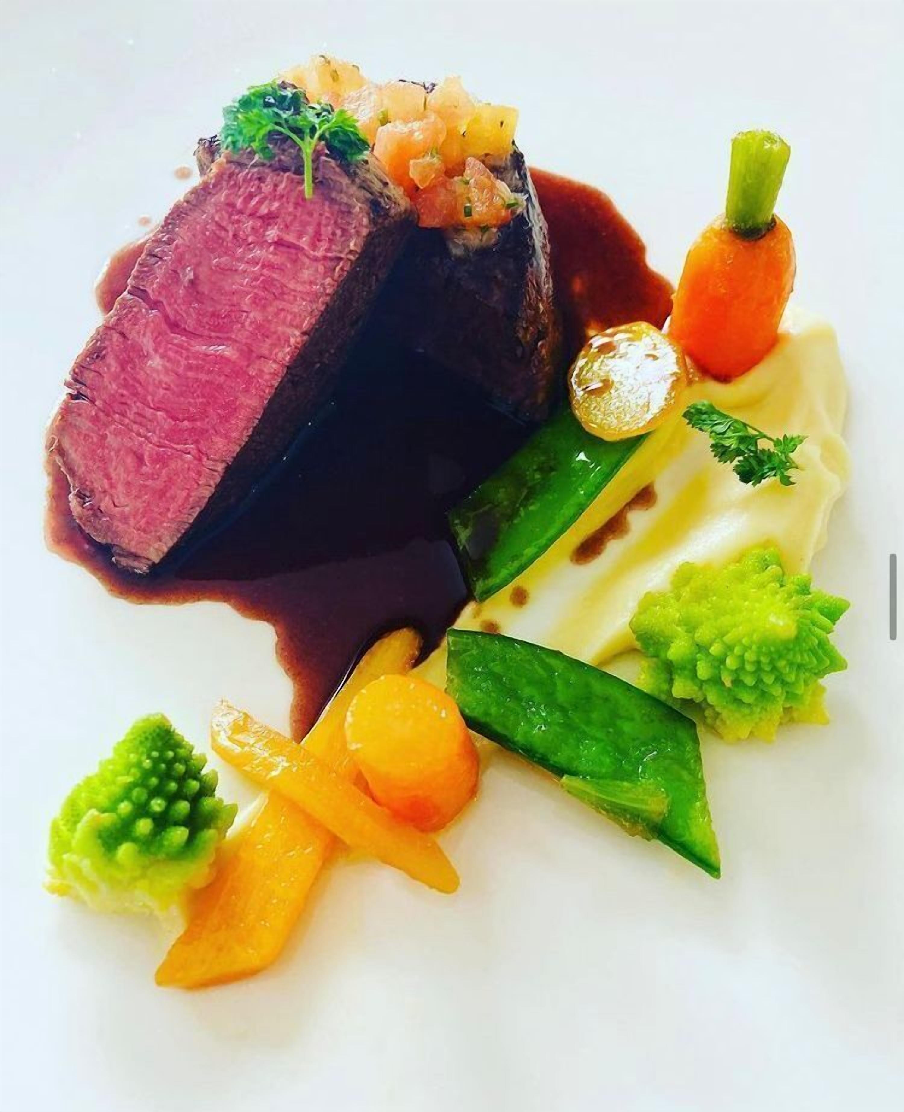 A plated dish with a slice of meat, vegetables, and a sauce.