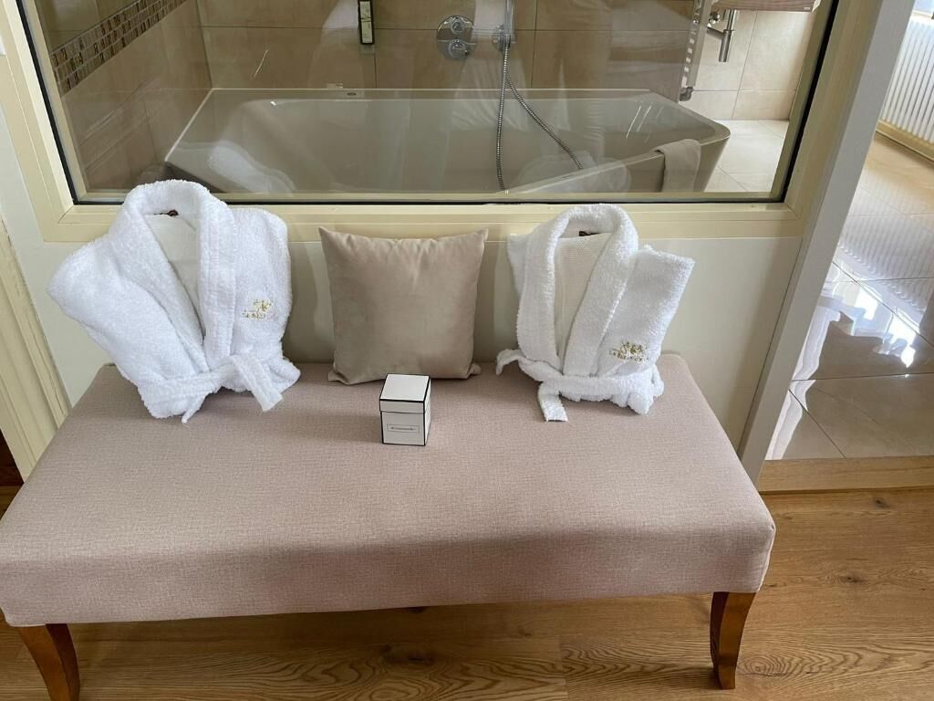 A bench with three white bathrobes and a small white box in a room with a glass shower area visible through a window.