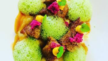 A dish with green spheres, meat, and pink garnish on a white plate.