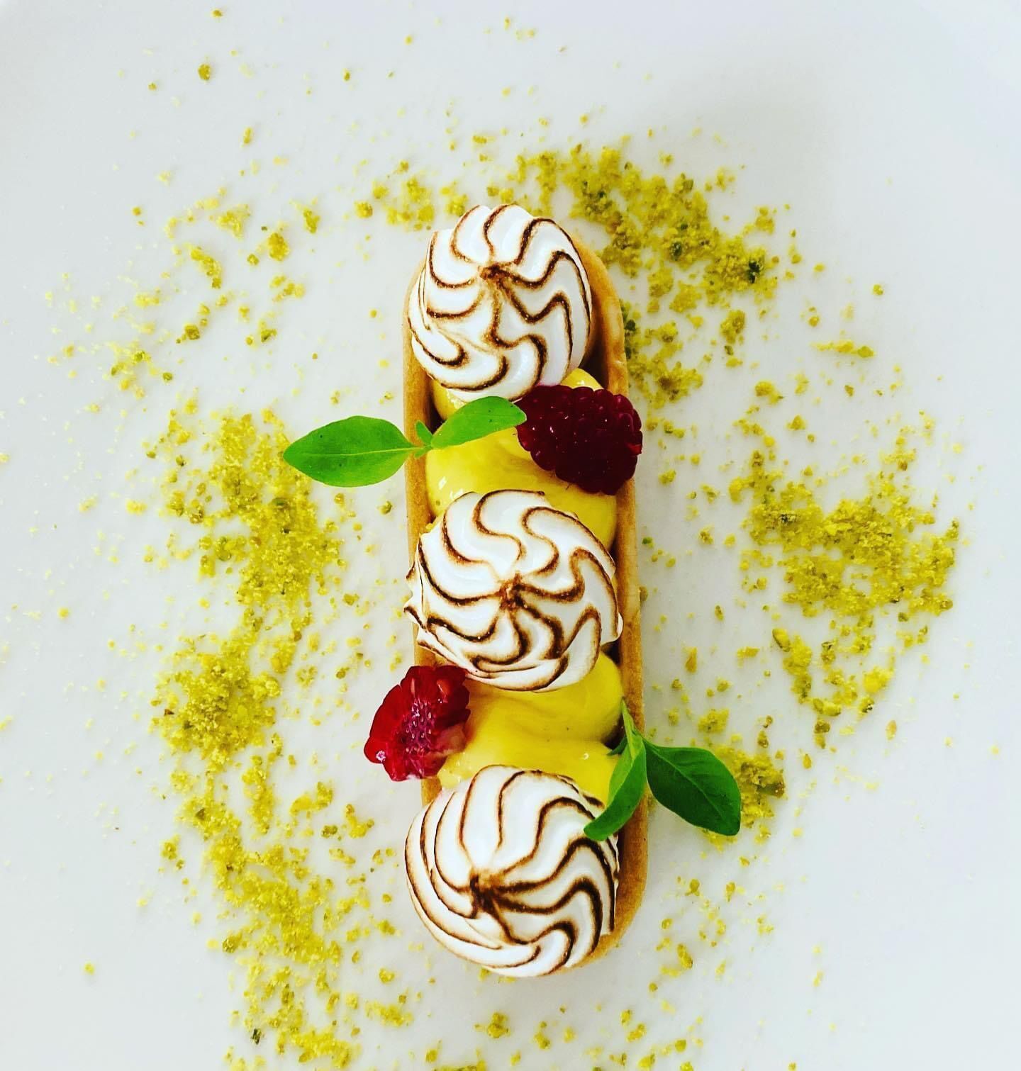 A dessert with whipped cream swirls, raspberries, and a green leaf garnish on a white plate.