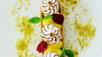 A dessert with whipped cream swirls, raspberries, and a green leaf garnish on a white plate.