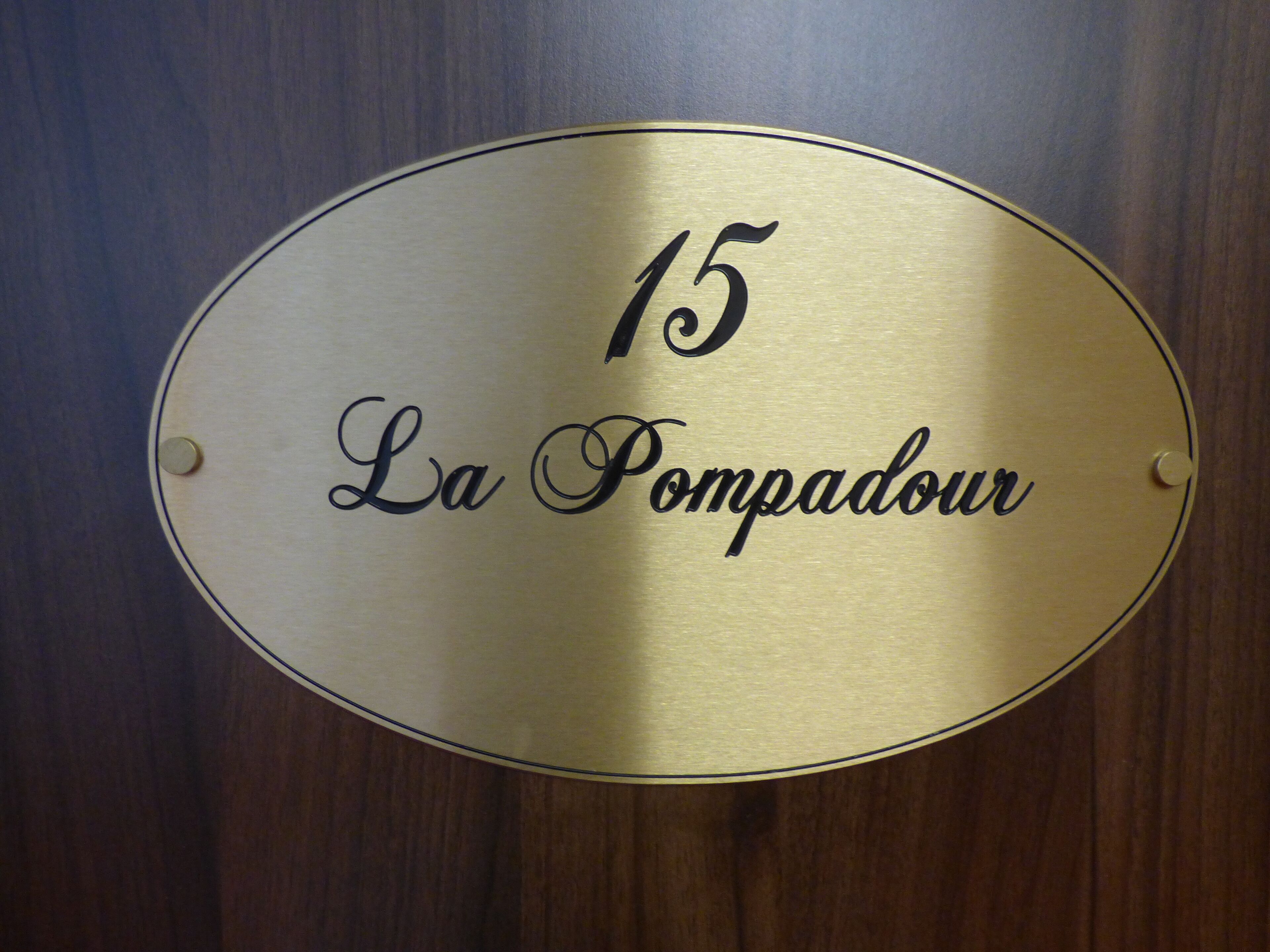 Una placa de latón con el número 15 y el texto 'La Pompadour' sobre una superficie de madera.