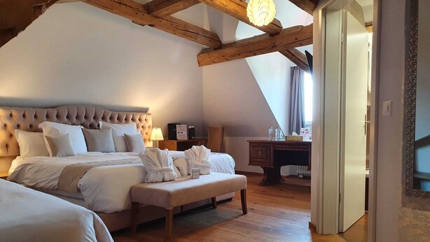 A bedroom with a large bed, a wooden bench, and a desk with a lamp. - Hotel La Belle Croix (Romont)