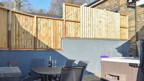 Eine Terrassenfläche mit Tisch, Stühlen, einer Weinflasche und einem Grill.