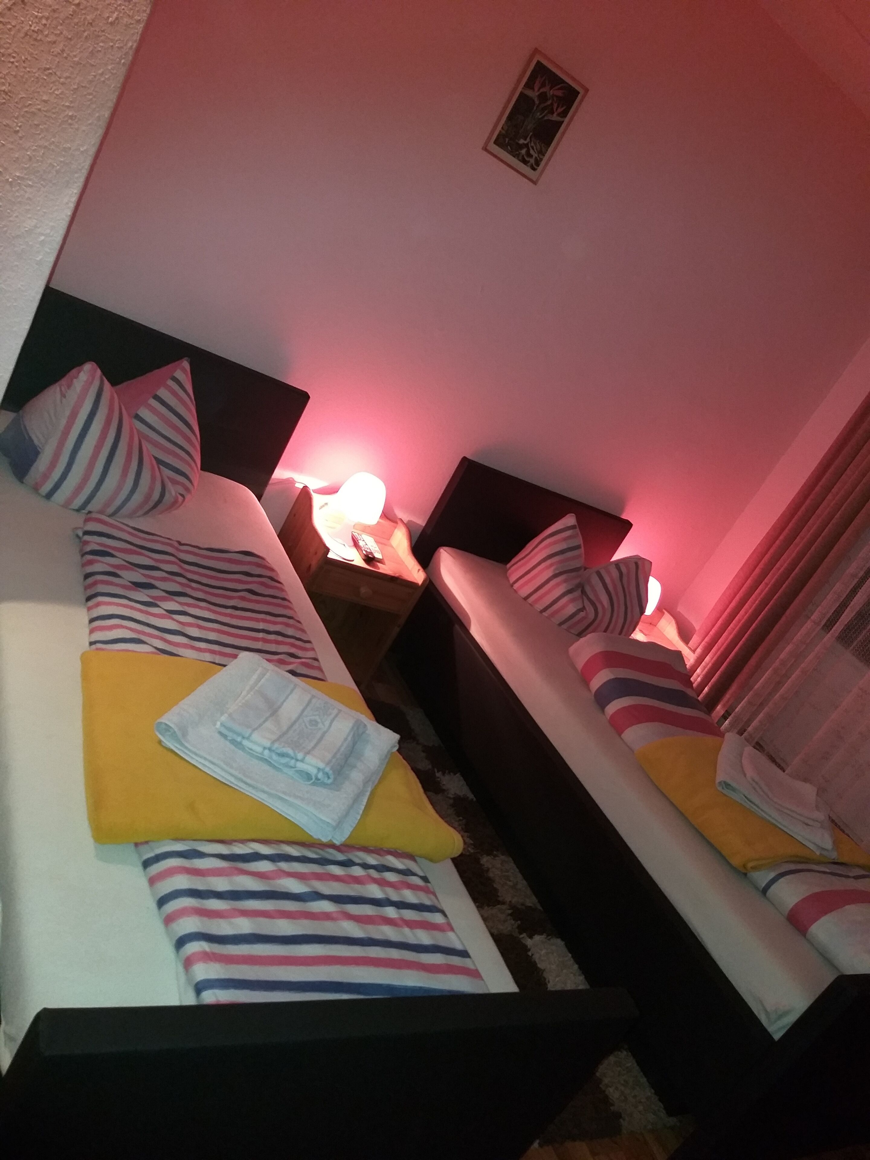 A hotel room with two beds, each with striped bedding and pillows. There is a nightstand with a lamp and a remote control.