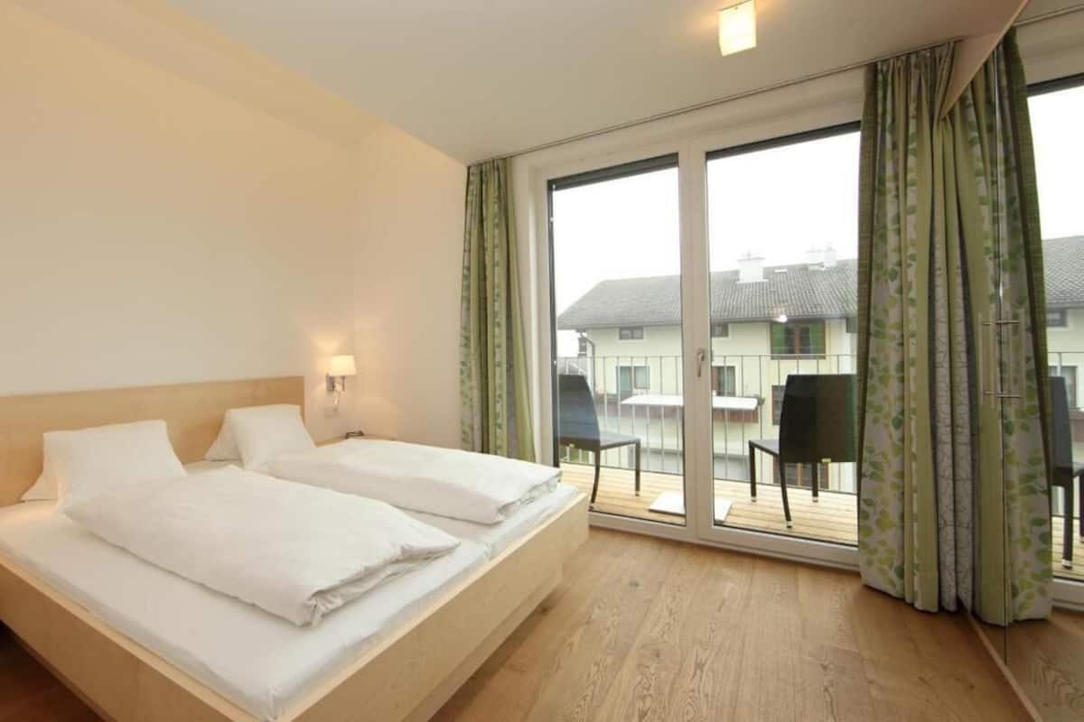 Une chambre d’hôtel avec un grand lit, deux tables de chevet, une fenêtre avec des rideaux et une vue sur l’extérieur.