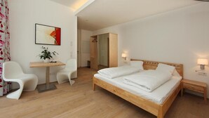 A modern hotel room with a wooden bed, a desk, two chairs, a mirror, and a painting on the wall.