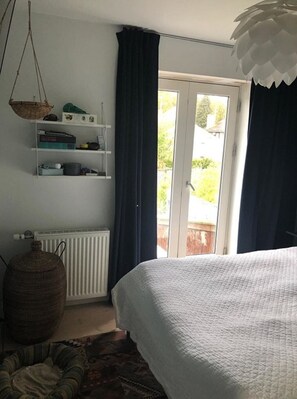 Une chambre à coucher avec un lit, un radiateur, une étagère avec des objets et une vue à travers une porte.