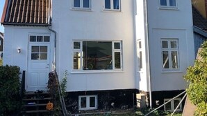 Un edificio residenziale a due piani con facciata bianca, tetto a falde e una porta d'ingresso ben visibile.