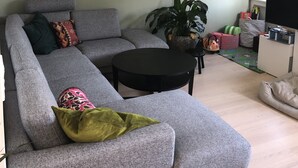 Un soggiorno con un divano angolare grigio, un tavolino da caffè nero, un lampadario a parete e una televisione.