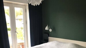 Una camera da letto con un letto, una scrivania, una lampada e vista attraverso una porta.
