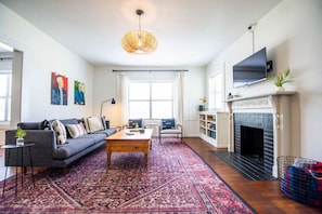 A living room with a sofa, coffee table, fireplace, TV, and artwork on the wall. - Cozy Tudor Bungalow in Waco (Waco)