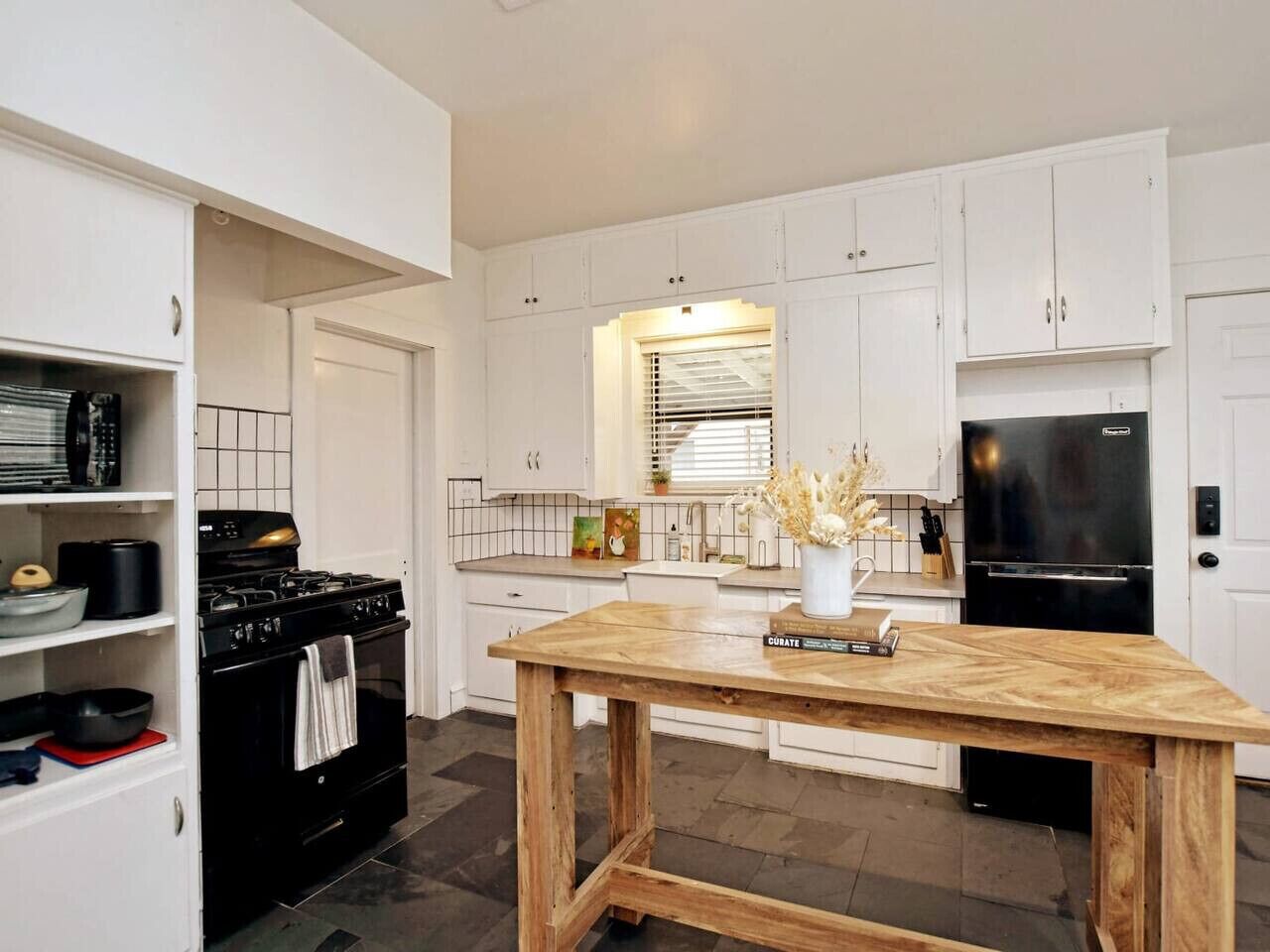 A modern kitchen with white cabinetry, a wooden table, a black stove, and a black refrigerator.