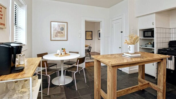 A modern kitchen with a dining area, featuring a coffee machine, a white table, and a wooden table. - Cozy Tudor Bungalow in Waco (Waco)