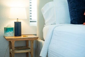 A neatly made bed with white linens, a bedside lamp, a tissue box, and a small wooden nightstand with a step. - Cozy Tudor Bungalow in Waco (Waco)