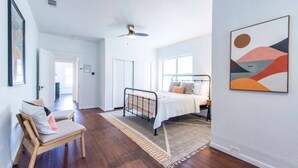 A bedroom with a bed, a chair, a ceiling fan, and a painting on the wall. - Cozy Tudor Bungalow in Waco (Waco)