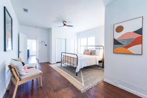 Una camera da letto con un letto, una poltrona, una ventola a soffitto e un quadro appeso al muro.
