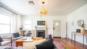 A living room with a sofa, coffee table, fireplace, television, and a bookshelf. - Cozy Tudor Bungalow in Waco (Waco)