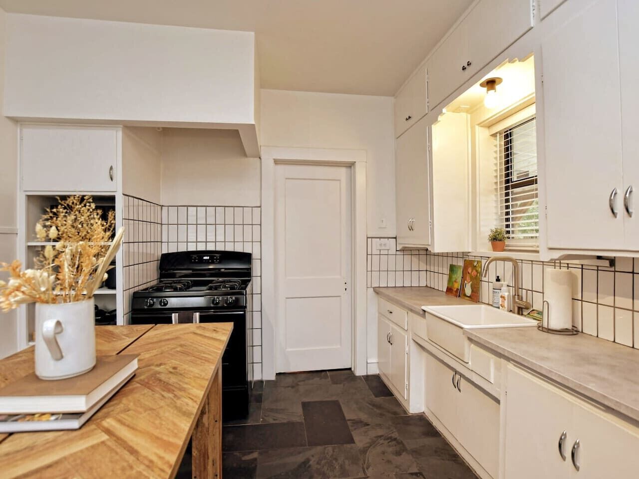 A kitchen with white cabinets, a stove, a sink, and a wooden table with a vase.