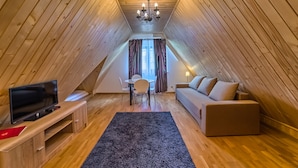 A cozy attic room with a wooden ceiling, a TV on a wooden stand, a sofa, a small table with chairs, and a chandelier. - Aparthotel Delta Bialka (Bukowina Tatrzanska)