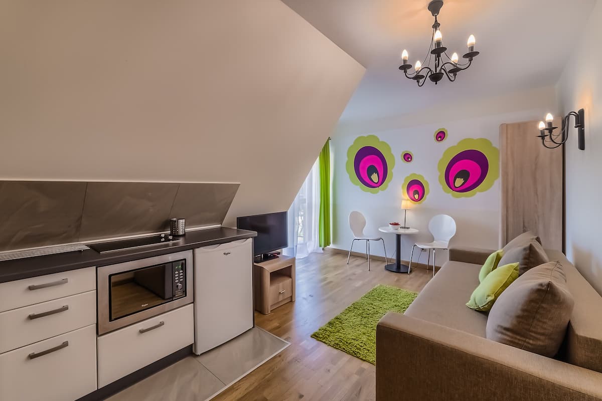 A modern kitchen with a microwave, a TV, and a small cabinet. There is a dining area with a table and chairs, and a sofa with cushions.